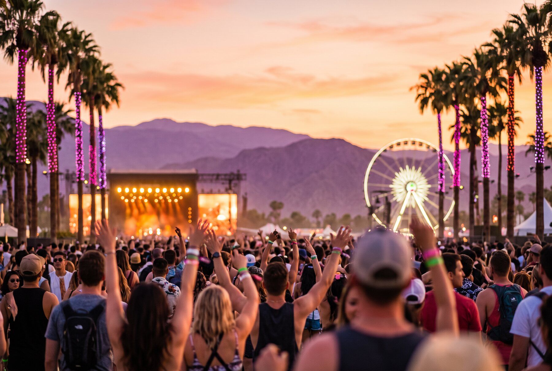 Desert music festival crowd at sunset with a Ferris wheel and lit palms